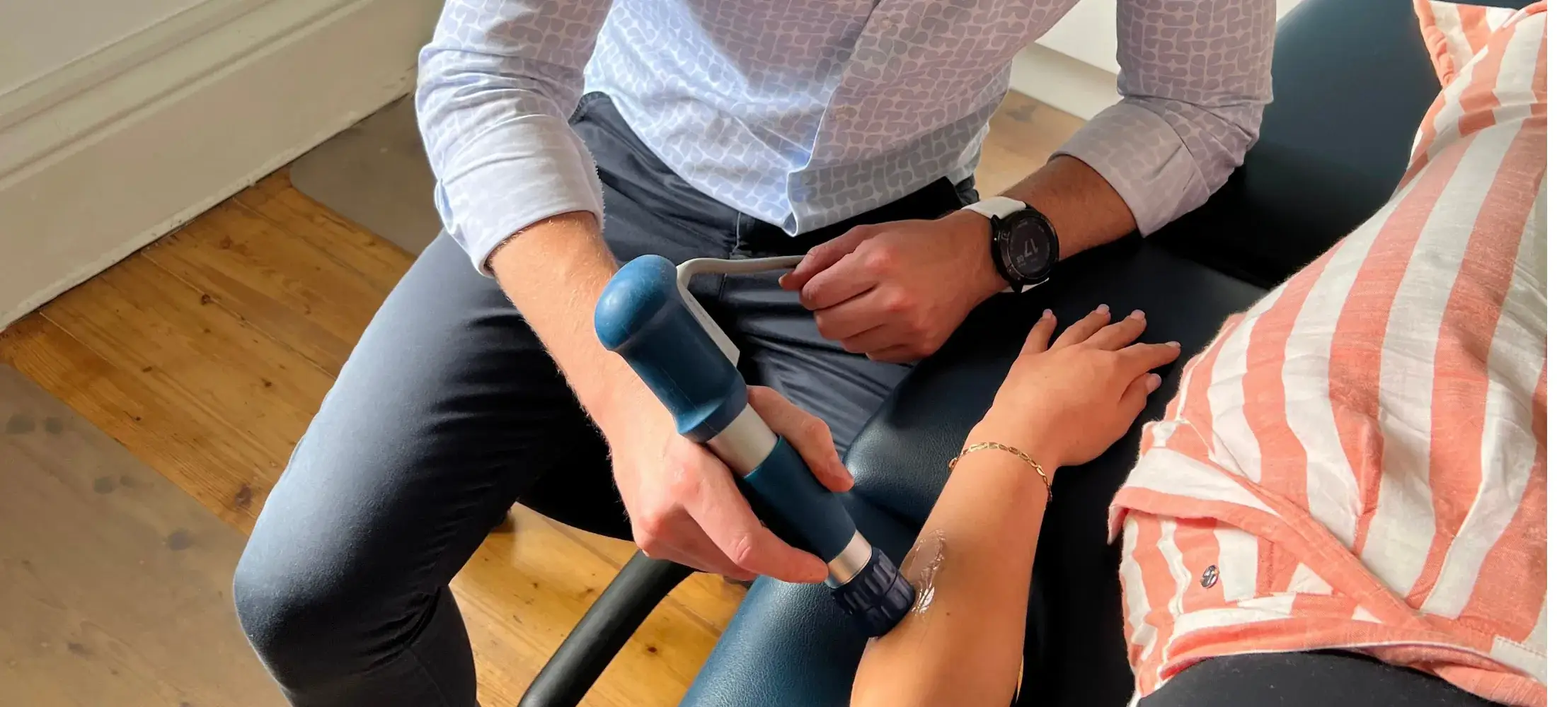 A shockwave therapy handpiece being applied to a patient's forearm